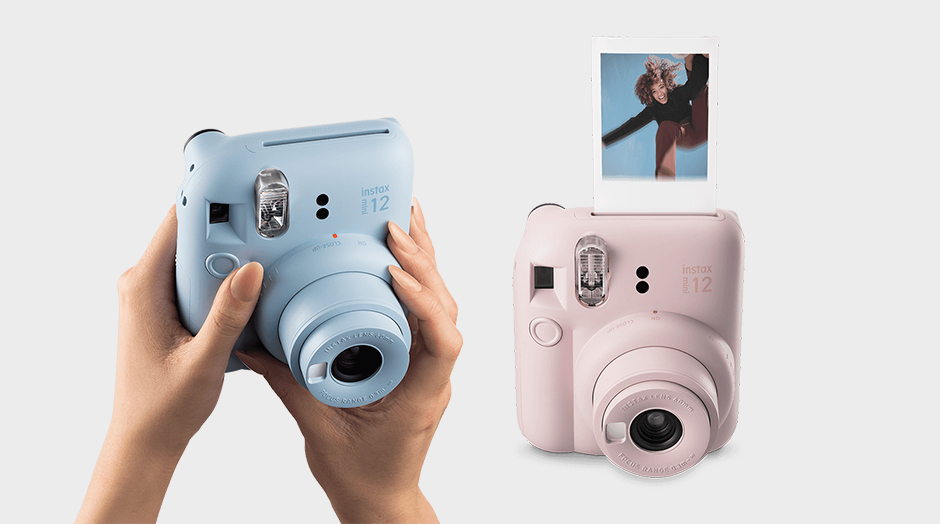 duas mquinas fotogrficas instax mini 12 da fujifilm, uma azul e outra rosa na mo com foto