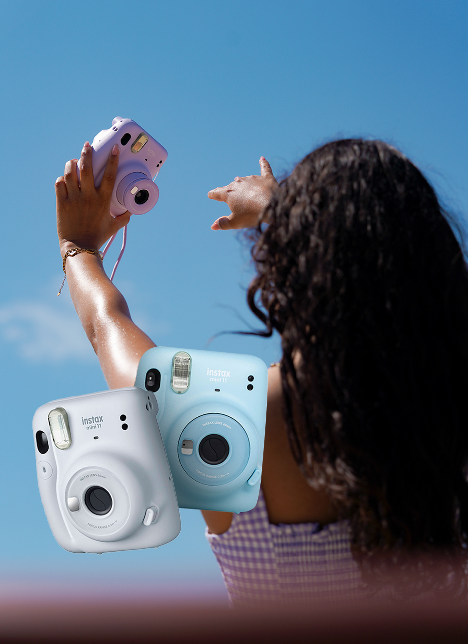 mulher a tirar selfie na praia com instax lilas e instax azul e branca ao lado